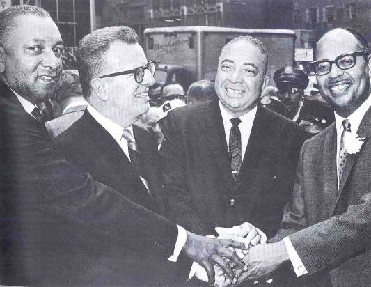 Photograph showing Postmaster Leslie Shaw, Postmaster General Lawrence O'Brien, Postmaster Henry McGee and Postmaster John Strachan participating in a group handshake in 1967.