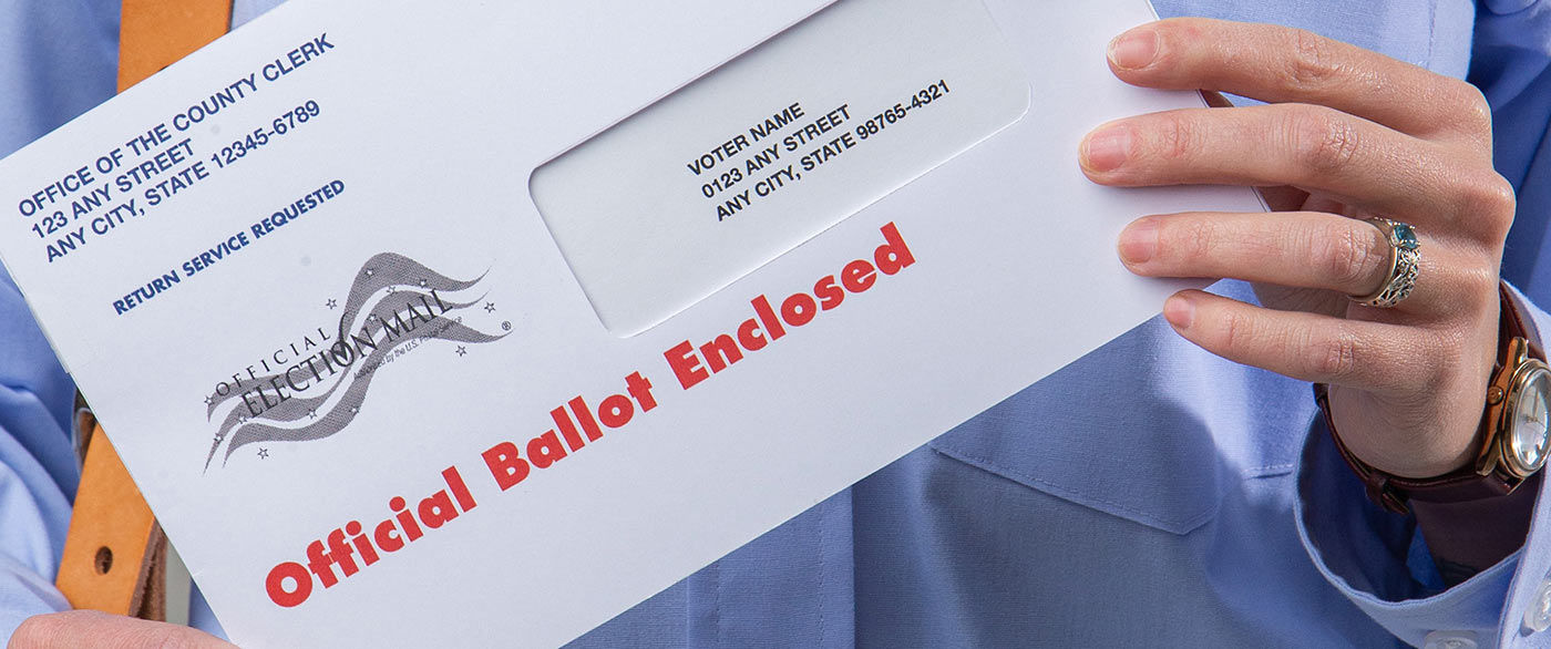 USPS employee holding an envelope containing an election ballot